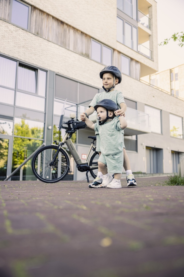 broertje loopt met broer voor fiets met fietshelmen